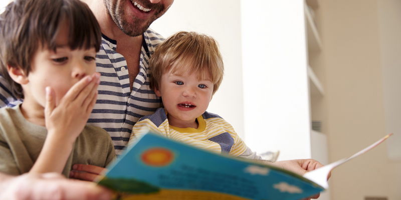 Kinder lesen mit dem Vater ein englisches Kinderbuch (Foto: Monkey Business Images/Shutterstock.com)
